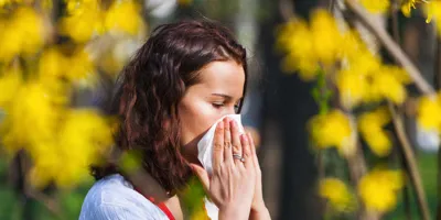Una mujer joven estornudando en un pañuelo en un campo lleno de flores silvestres con una alta concentración de polen