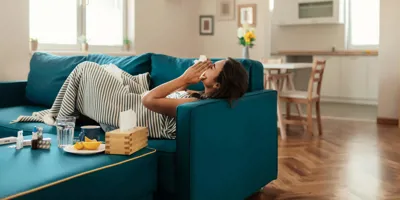 Una chica tumbada en un sofá de color azul sonándose con un pañuelo de papel.