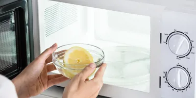 Unas manos sujetando un recipiente con medio limón e introduciéndolo en un microondas.