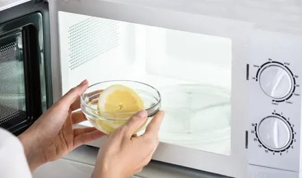 Unas manos sujetando un recipiente con medio limón e introduciéndolo en un microondas.