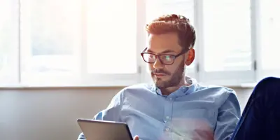 Un hombre con gafas sentado utilizando una tablet. 