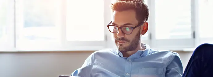 Un hombre con gafas sentado utilizando una tablet.