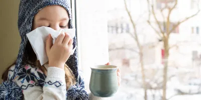  Una niña pequeña con ropa de invierno sonándose la nariz con un pañuelo de papel. 