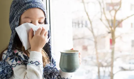  Una niña pequeña con ropa de invierno sonándose la nariz con un pañuelo de papel. 