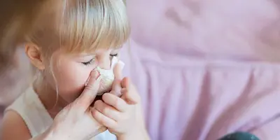 Una madre ayudando a su hija a sonarse la nariz con un pañuelo de papel