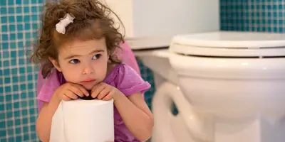 Una niña sentada en un baño mirando pensativa con un rollo de papel higiénico.
