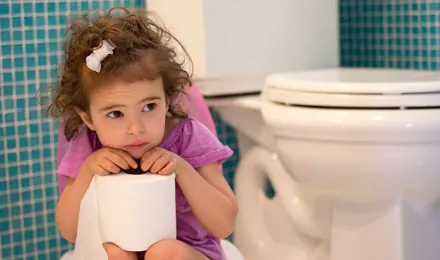Una niña sentada en un baño con un rollo de papel higiénico en sus manos