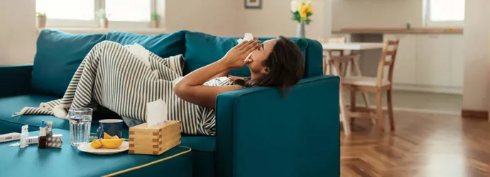 Una chica tumbada en un sofá de color azul sonándose con un pañuelo de papel.