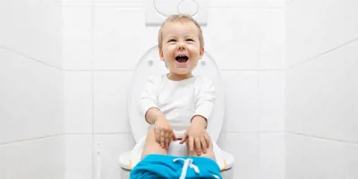 Un niño pequeño riéndose sentado en un inodoro para hacer popó.
