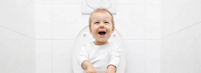 Un niño pequeño riéndose sentado en un inodoro para hacer popó.