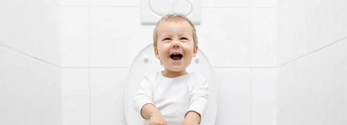 Un niño pequeño riéndose sentado en un inodoro para hacer popó.
