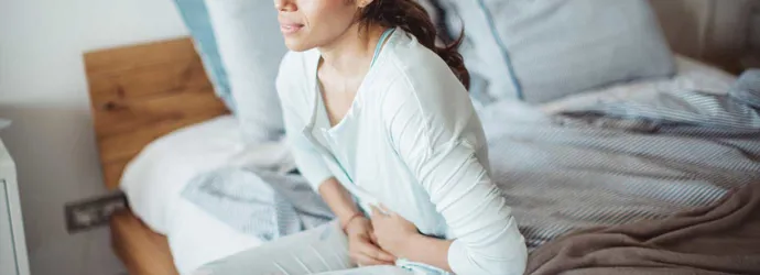 Una mujer sentada en su cama con dolor de estómago a causa de la diarrea.