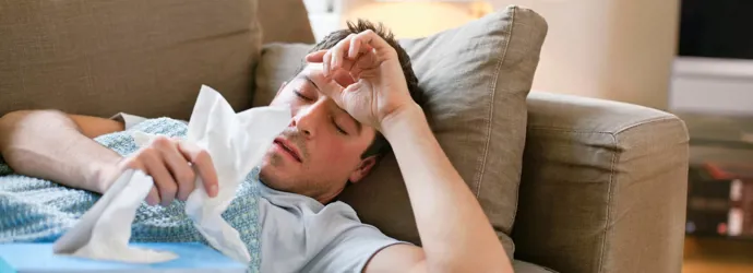 Hombre tumbado en el sofá con gripe masculina con pañuelos