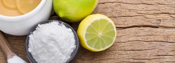 Productos de limpieza ecológicos como el limón, la lima, y el bicarbonato de sodio en una tabla de cortar de madera