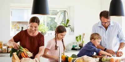 Una madre y un padre enseñando reciclaje para niños, desempaquetando comida de envases reciclables en una cocina