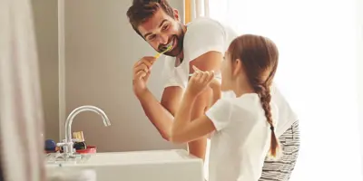 Un hombre y su hija aprendiendo a ahorrar agua mientras se cepillan los dientes juntos en un cuarto de baño