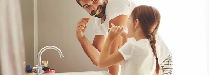 Un hombre y su hija aprendiendo a ahorrar agua mientras se cepillan los dientes juntos en un cuarto de baño