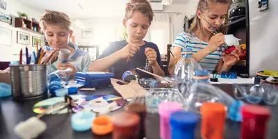 3 niños aprendiendo a reducir los residuos mediante la elaboración de manualidades de plásticos reciclables y tubos de cartón