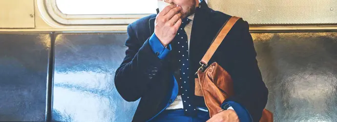 Um homem de fato sentado numa carruagem de comboio a assoar o nariz