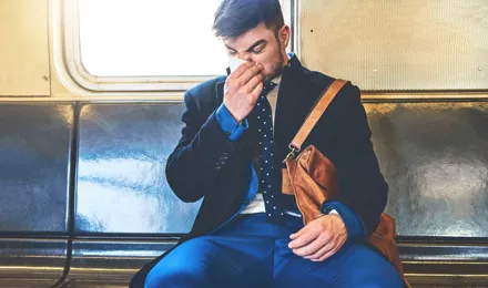 Um homem de fato sentado numa carruagem de comboio a assoar o nariz