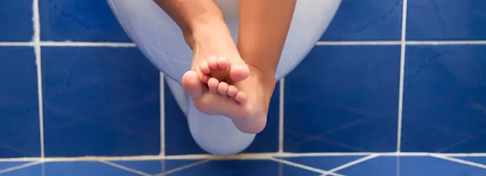 Os pés e pernas de uma criança pendurados numa sanita branca
