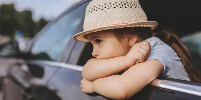 Criança enjoada num carro a usar um chapéu