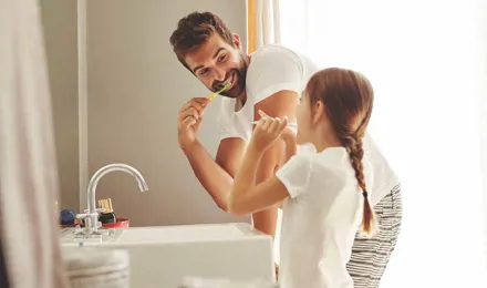 Um homem e a sua filha aprendem a economizar a água enquanto escovam os dentes juntos na casa de banho