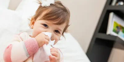 Menina a limpar o nariz com um lenço de papel