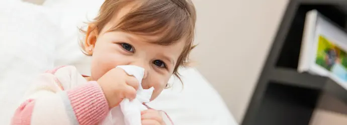 Menina a limpar o nariz com um lenço de papel