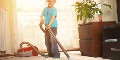 Um rapaz a limpar o tapete com um aspirador