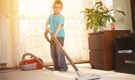 Um rapaz a limpar o tapete com um aspirador