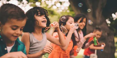 Un grupo de cinco niños haciendo pompas de jabón al aire libre.