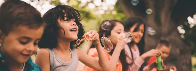 Un grupo de cinco niños haciendo pompas de jabón al aire libre.
