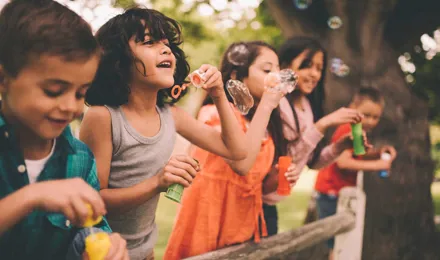 Un grupo de niños de pie sobre una valla de madera haciendo burbujas en verano