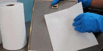 Una mujer con guantes de goma limpiando la campana extractora de la cocina.