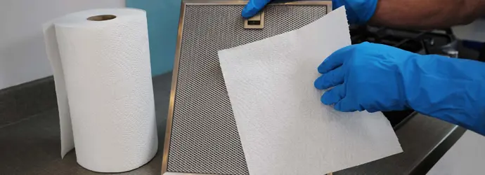 Una mujer con guantes de goma limpiando la campana extractora de la cocina.