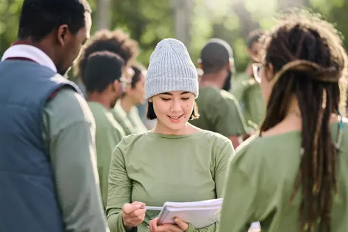 Una mujer sonriente, al aire libre, lee un documento a otras dos personas.