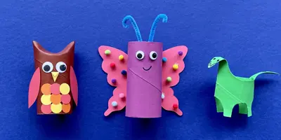 Una madre y su hija haciendo manualidades de animales con rollos de papel higiénico en el escritorio.