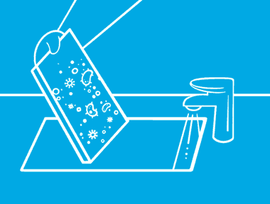 Unas manos sobre un fondo azul utilizando agua con jabón para eliminar las bacterias de una tabla de cortar.